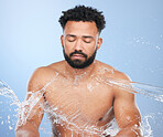 Skincare, water splash and man in studio for cleaning, hygiene or cosmetic care on blue background. Shower, face and topless male model relax with luxury hydration, pamper or bathroom beauty routine