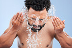 Black man, water splash and washing face for skincare, hygiene or grooming against a blue studio background. African male person, model and aqua for body hydration, shower or facial skin treatment