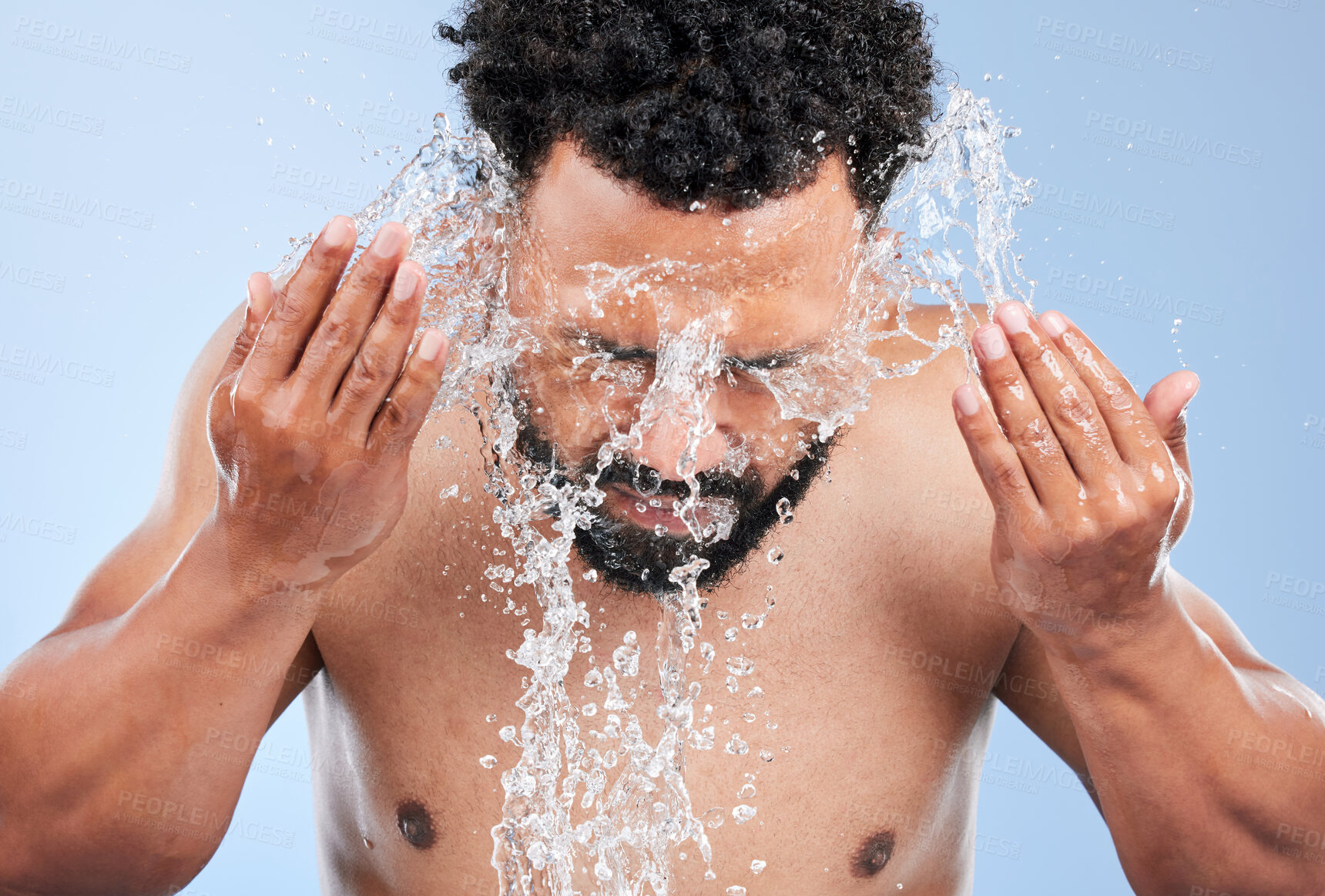 Buy stock photo Black man, water splash and washing face for skincare, hygiene or grooming against a blue studio background. African male person, model and aqua for body hydration, shower or facial skin treatment