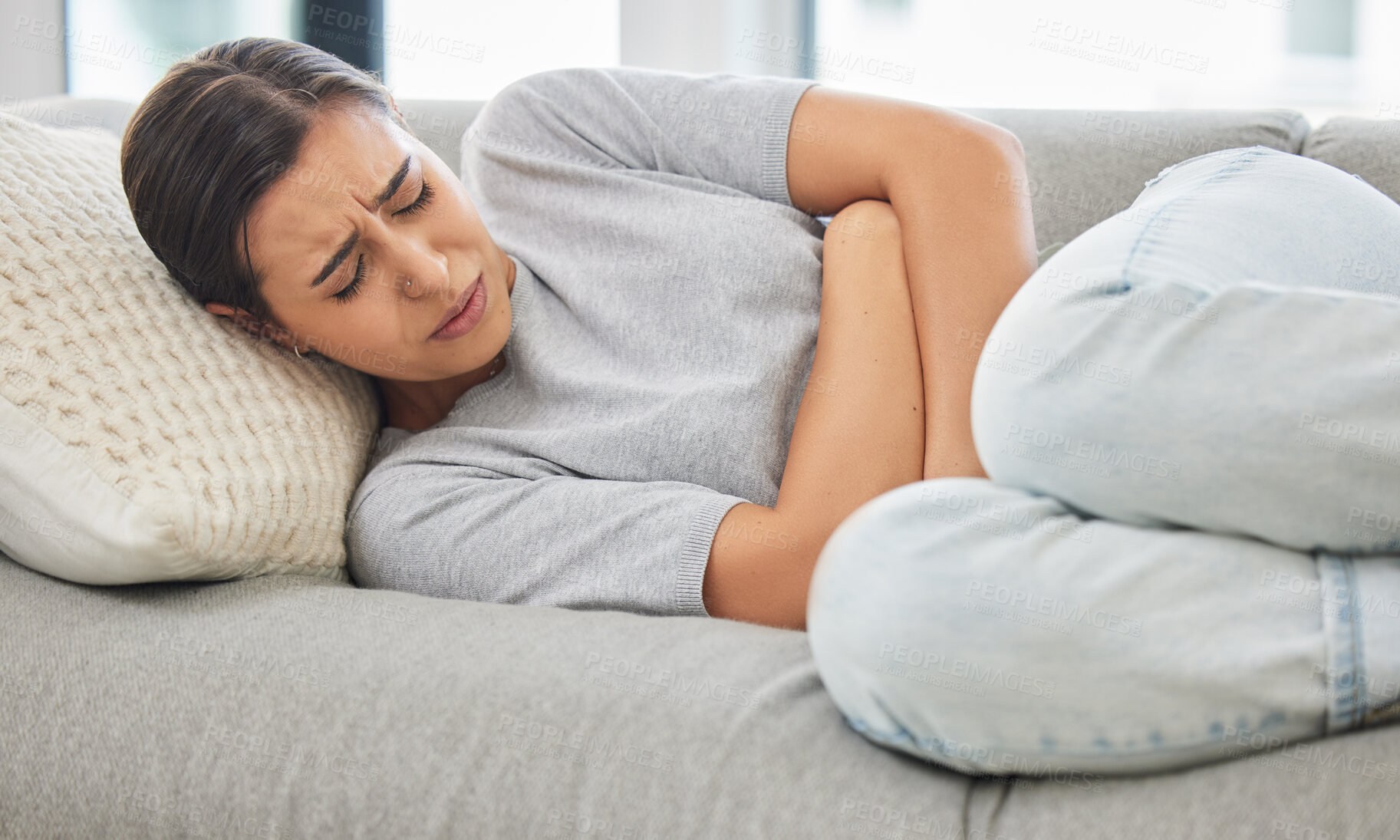 Buy stock photo Woman, stomach pain and stress on sofa, sick or menstruation with anxiety, gas or virus in home living room. Girl, abdomen and emergency for gut health, constipation or cramp on lounge couch in house