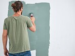 Painting, brush and renovation with a man doing interior DIY in a room for improvement and remodel of home. Young man, decoration and work with green paint on a wall to maintenance in domestic house
