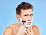 Man, razor and shaving for haircare, grooming and hair removal for hygiene on a blue studio background. Portrait, man and beauty to shave beard or face with foam or soap for facial cleansing