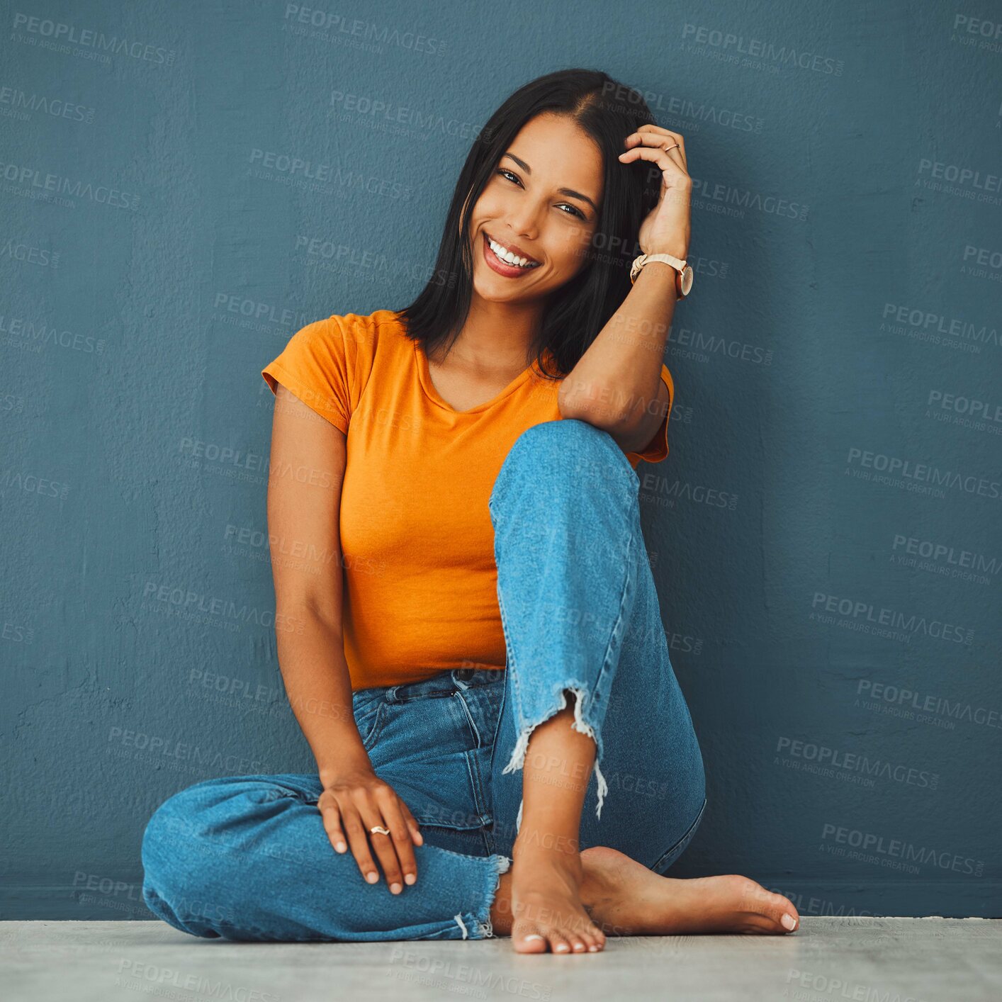 Buy stock photo Black woman, floor and home with smile by wall for clothes, relax and fashion with barefoot. Gen z girl, model portrait and happy in house with feet, jeans and happiness on face by blue background