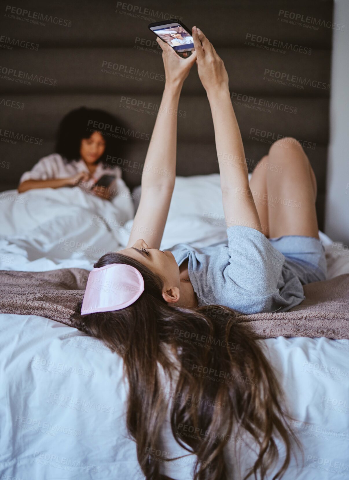 Buy stock photo Video call, phone and relax with woman at sleepover for communication, internet and contact. Happy, online dating and smile with girl and friends in bedroom with technology, digital and social media