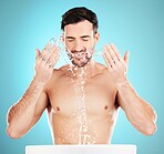 Water splash, skincare and man cleaning face, morning detox treatment isolated on blue background. Facial hygiene, male model with tattoo and grooming for health, wellness and skin care in studio.