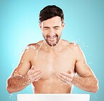 Water splash, facial skincare and man with cleaning face, morning detox treatment isolated on blue background. Hygiene, male model and grooming for health, wellness and skin care or beauty in studio.