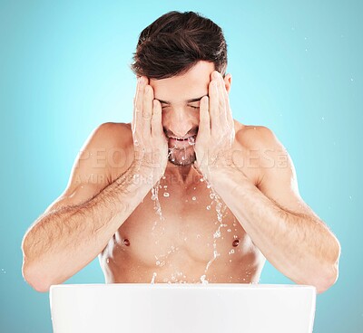 Water, skincare and man with cleaning face, morning skin treatment isolated on blue background. Facial hygiene, splash and male model with tattoo grooming for health, wellness and beauty in studio.