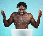 Water splash, cleaning and hydration with a model black man in studio on a blue background for hygiene. Bathroom, skincare and wellness with a young male washing his face for natural skin treatment