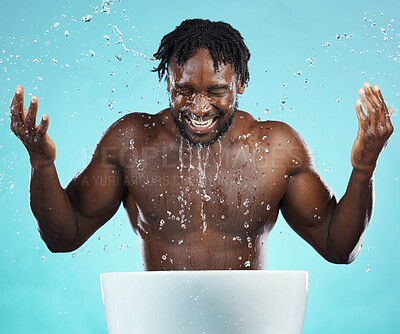 Buy stock photo Water splash, cleaning and hydration with a model black man in studio on a blue background for hygiene. Bathroom, skincare and wellness with a young male washing his face for natural skin treatment