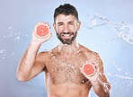 Grapefruit, water splash and man on blue background for wellness benefits, beauty and skincare. Male model, portrait and citrus fruits for vitamin c cosmetics, detox and nutrition for healthy shower