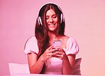 Pink, light and music by woman in a bed with headphones, social media and streaming on wall background. Podcast, texting and girl relax in bedroom, happy and enjoying radio, audio or online playlist