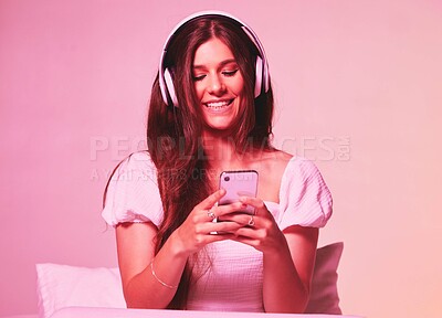 Buy stock photo Pink, light and music by woman in a bed with headphones, social media and streaming on wall background. Podcast, texting and girl relax in bedroom, happy and enjoying radio, audio or online playlist