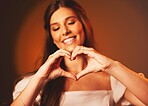 Woman, hand heart sign and love symbol of a happy female person in studio. Smile, happiness and loving emoji hands gesture with brown background and gen z model ready for a valentines day date