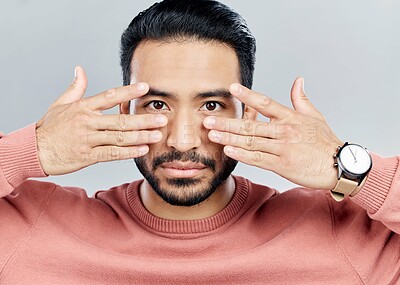 Buy stock photo Portrait, eyes and vision with a man in studio on a gray background making a masquerade hand gesture. Face, hands and focus with a handsome young male posing against a wall while touching his cheeks