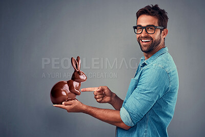 Buy stock photo Portrait, smile and man pointing at chocolate rabbit in studio isolated on grey background. Face, glasses and person gesture at bunny, food and sweets, candy and eating for easter holiday celebration