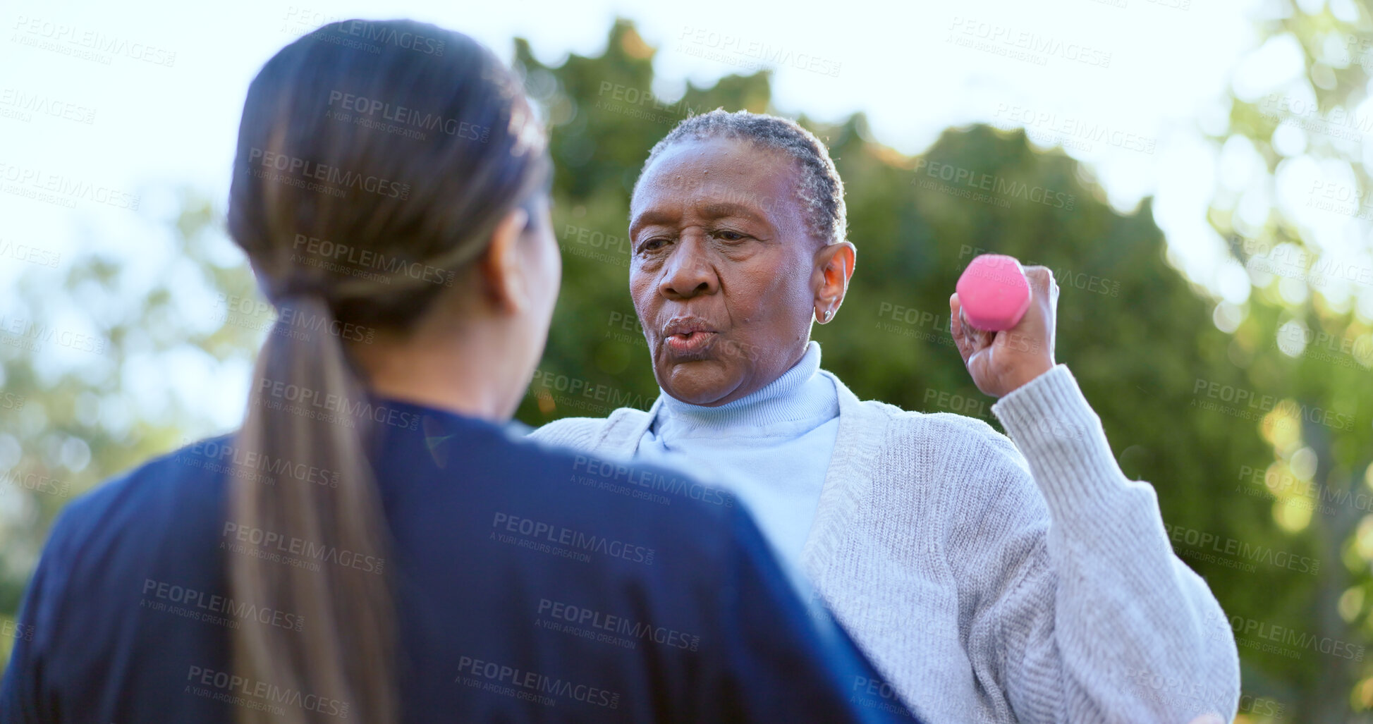 Buy stock photo Dumbbell, fitness and a senior black woman with a volunteer outdoor in a garden together for physiotherapy. Exercise, health or wellness with an elderly patient and nurse in the yard to workout