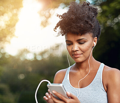 Buy stock photo Shot of a young woman listening to music on her phone while out for a run
