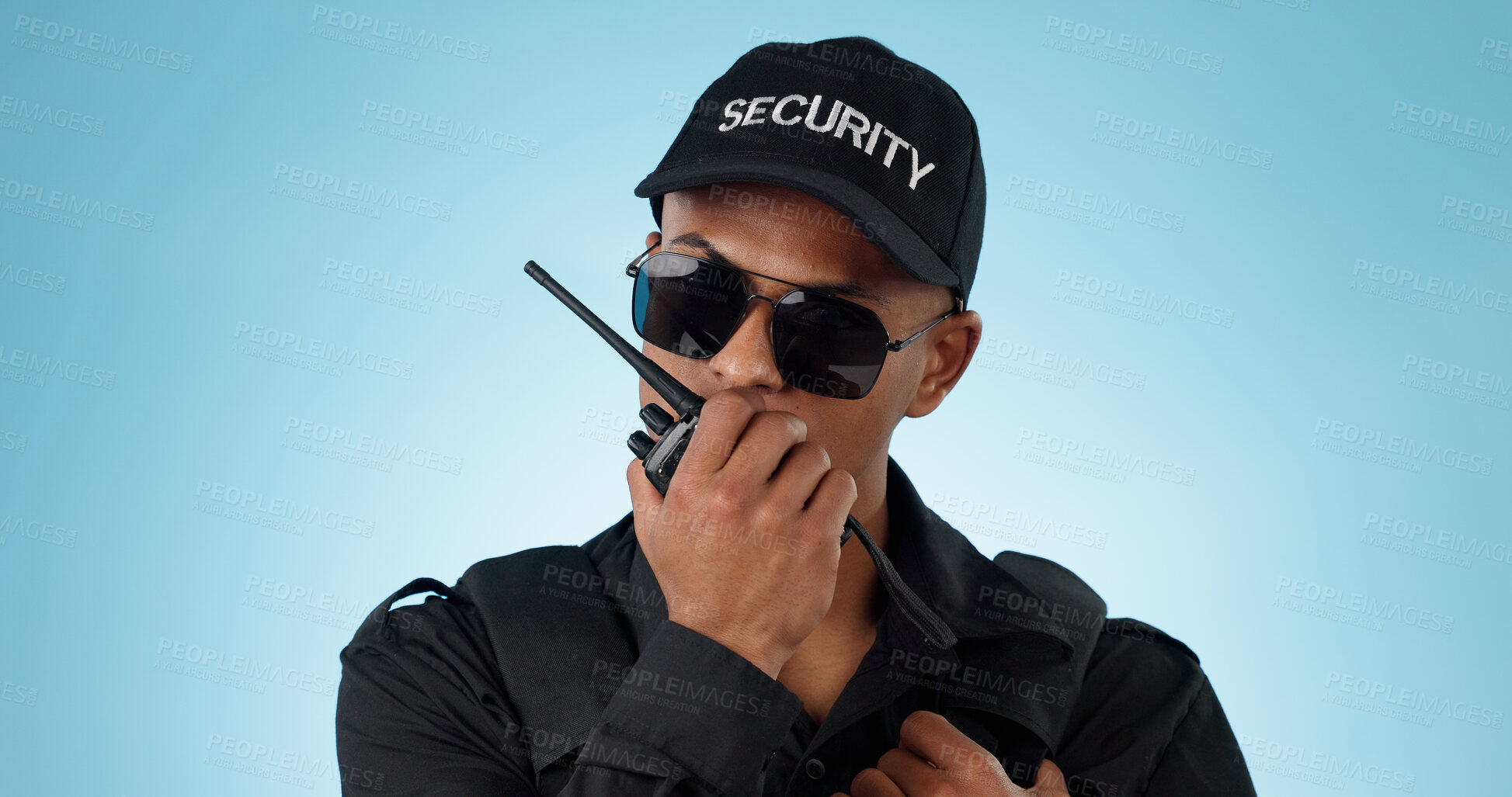 Buy stock photo Security, radio and an officer man on a blue background in studio for surveillance or communication. Face, uniform and sunglasses with a young law person speaking on a walkie talkie for patrol