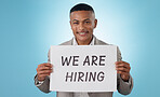 Portrait, happy or businessman with we are hiring sign, work opportunity or vacancy advertising in studio. Smile, poster or manager with board text for job search or recruitment on blue background