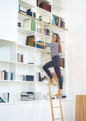 Buy stock photo Portrait of a smiling young woman climbing a ladder on a bookshelves at home