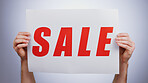 Sale, sign and hands with a poster, promotion and announcement of discount in studio with white background. Retail, shopping and person advertising with news, banner and deal for commercial savings