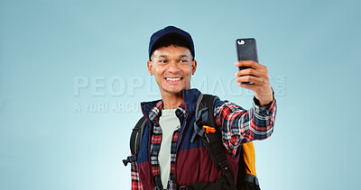 Buy stock photo Man, hiking selfie and smile in studio with backpack, gear and post on web blog by blue background. Influencer person, camping or trekking with photography for memory, profile picture or social media