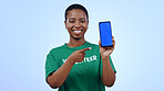 Woman, volunteering and point at phone with green screen in portrait for mockup on blue background in studio. Black person, happy or smile for internet, cellular or network for homepage on mobile app