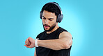 Man, headphones and checking watch in fitness for performance against a blue studio background. Male person, athlete or model looking at wristwatch for monitoring or tracking steps on mockup space