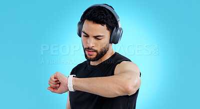 Buy stock photo Man, headphones and checking watch in fitness for performance against a blue studio background. Male person, athlete or model looking at wristwatch for monitoring or tracking steps on mockup space