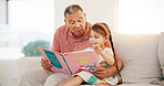 Grandpa, child and reading book on sofa for literature, education or bonding together at home. Grandparent with little girl or kid smile for story, learning or relax on living room couch at house