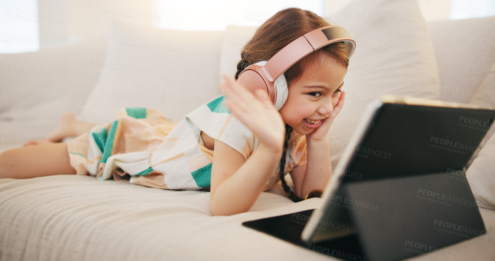 Buy stock photo Happy girl, tablet and headphones on sofa for video call, elearning or streaming at home. Female child or kid smile and wave with technology in relax for virtual class, education or learning at house