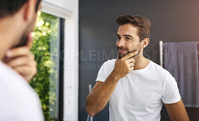 Buy stock photo Cropped shot of a handsome man rubbing his beard and looking in the mirror at home