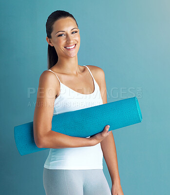 Buy stock photo Studio portrait of a healthy young woman holding an exercise mat against a blue background
