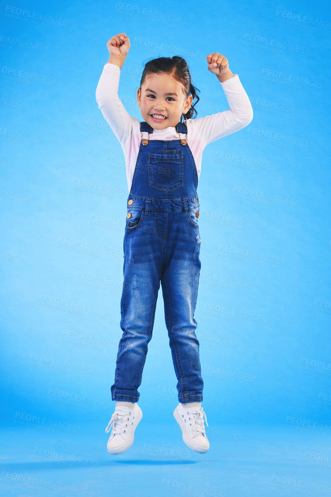 Buy stock photo Jump, smile and portrait of a child in a studio with energy, achievement or good news with excitement. Happy, youth and full length of a girl kid model moving for winning by isolated blue background.