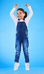 Girl child, jump and celebration in studio with fist in air for goal, achievement or success by blue background. Female kid, excited winner and champion with yes, energy or motivation for competition