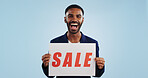 Excited man, portrait and sale sign for advertising, deal or discount against a blue studio background. Happy male person showing billboard or poster for marketing, promotion or special on mockup