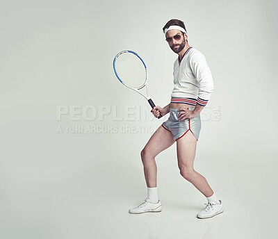 Buy stock photo A young man in the studio wearing ill-fitting retro tennis wear and shades while holding a racquet