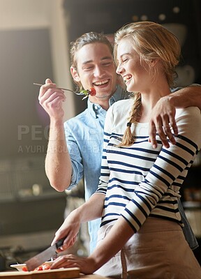 Buy stock photo Shot of a young man feeding his girlfriend some of the salad she's preparing