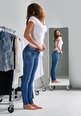 Buy stock photo Shot of an attractive young woman trying on jeans in a mirror