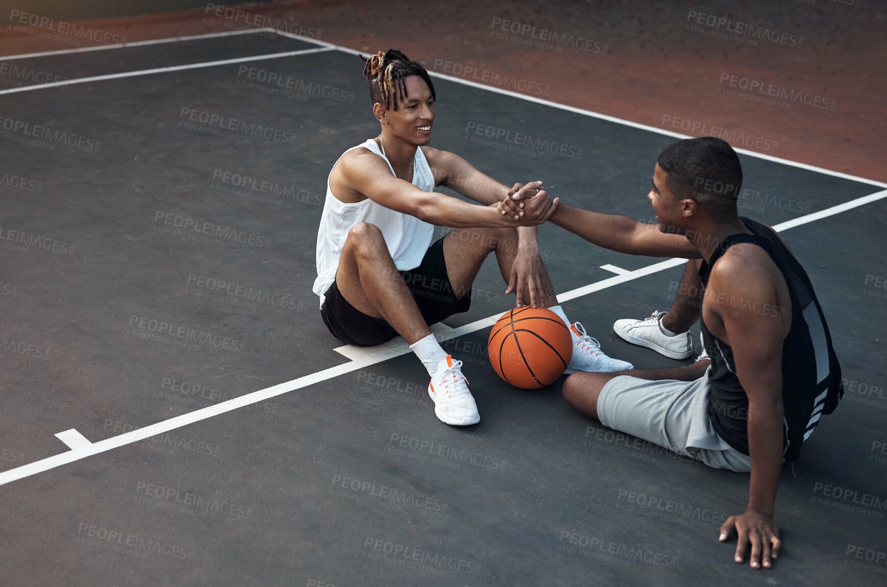 Buy stock photo Shot of two sporty young men shaking hands on a basketball court