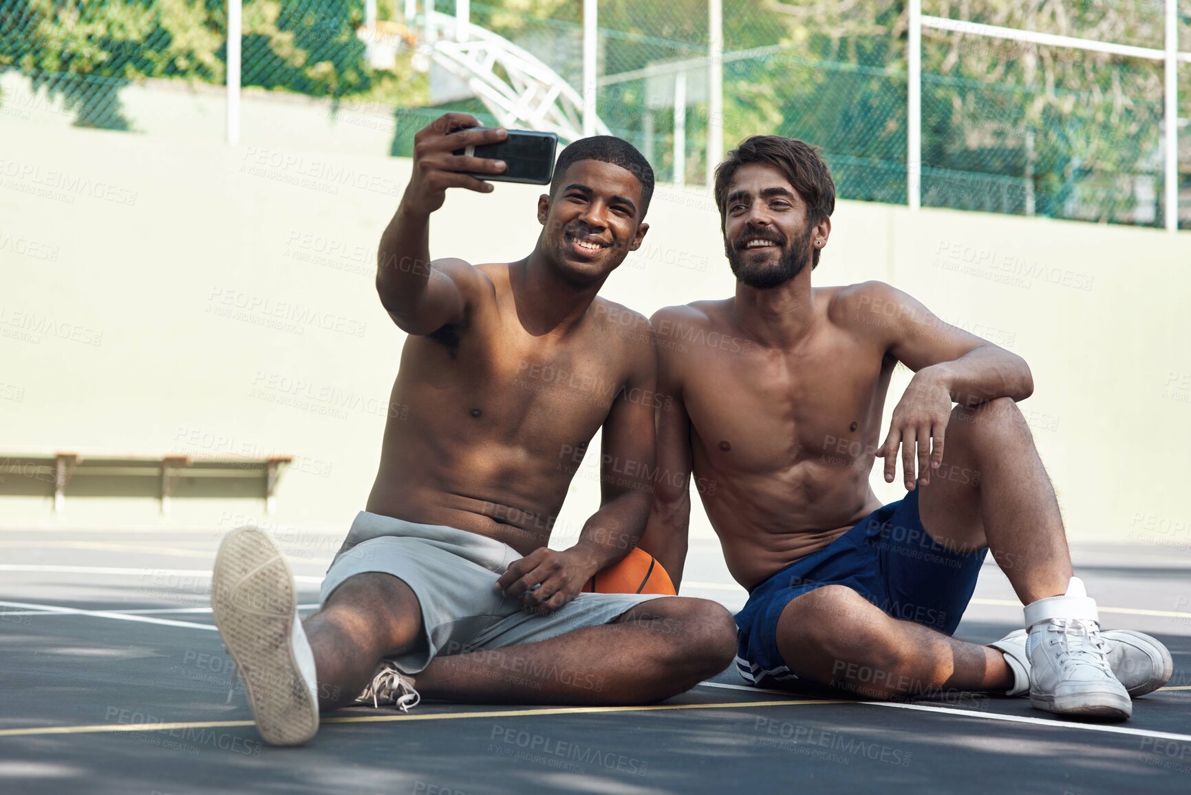Buy stock photo Shot of two sporty young men taking selfies on a basketball court