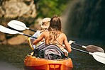 Women friends rowing a kayak or boat on a river or lake while on summer vacation or travel. Tourist explore nature on water during a tropical adventure kayaking in the a wildlife wilderness forest 