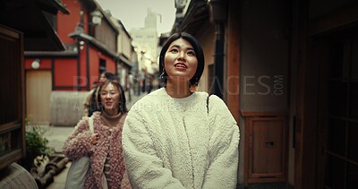 Women, friends and walk in street, talking and travel together on vacation, city and buildings. Japanese people, girl and chat outdoor in metro road, houses and urban neighborhood with ideas in Tokyo