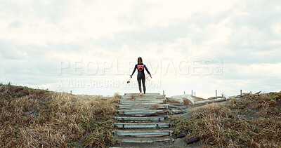 Woman, surfer with surfboard at beach and back view, nature and extreme sports for fitness. Athlete on stairs, exercise and surfing, workout or training with ocean, health and wellness with hobby