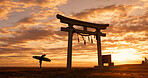 Torii gate, sunset and man with surfboard bowing, ocean and travel adventure in Japan with orange sky. Shinto architecture, Asian culture and calm beach in Japanese nature with person at spiritual monument.