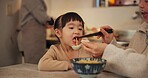 Family, Japanese and woman feeding daughter in kitchen of home for growth, health or nutrition. Food, girl eating in Tokyo apartment with mother and grandparent for diet or child development