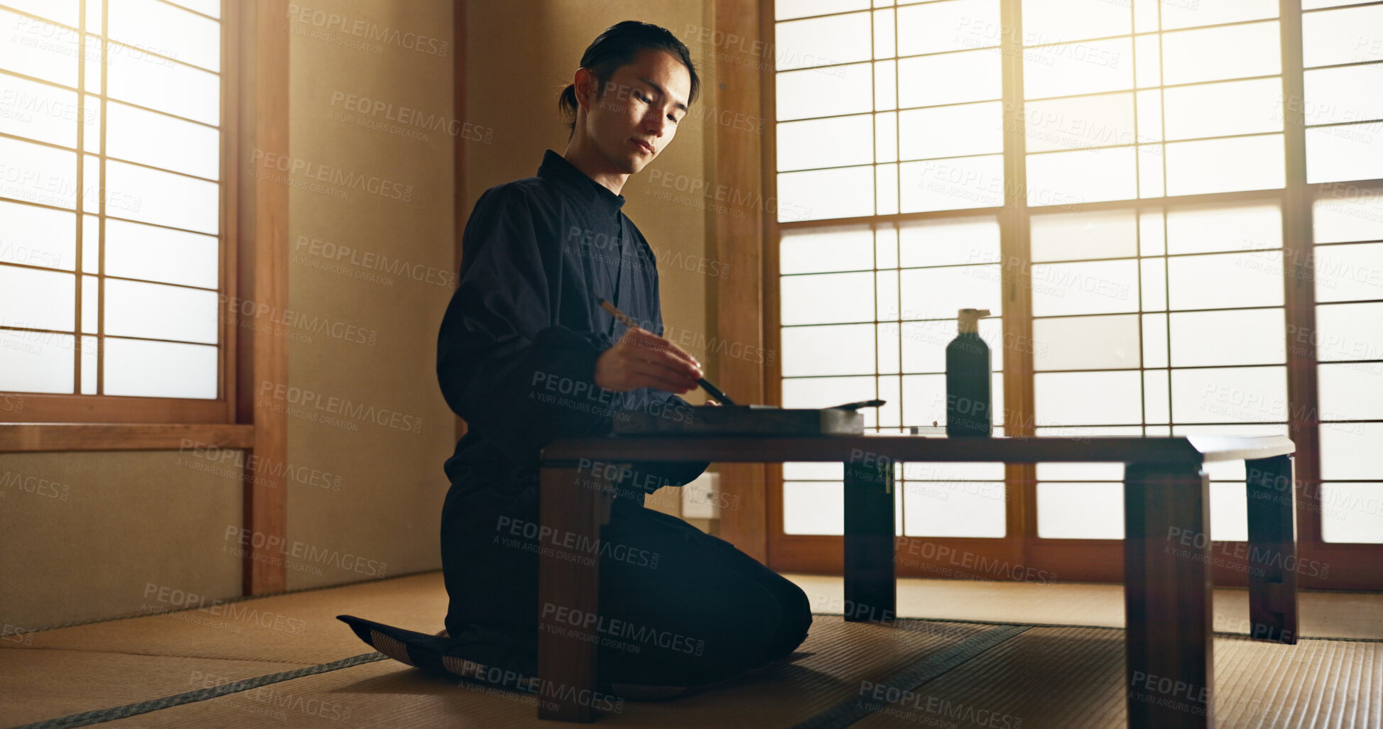 Buy stock photo Man, calligraphy or creative Japanese artist in studio for art and script, letter with table, paper or alphabet. Asian, brush or person with tools, paintbrush and focus with traditional stationery