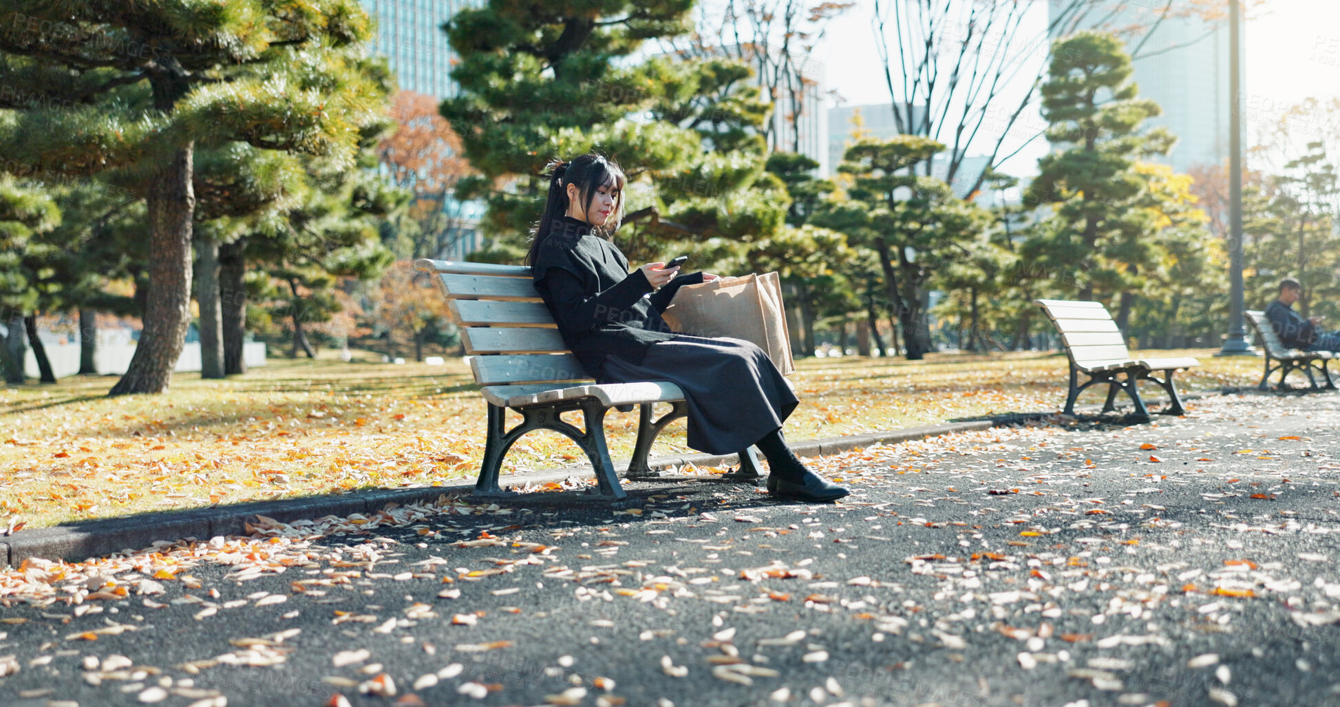 Buy stock photo Japanese woman, bench and smartphone in park with relax, happiness and social media in sunshine in city. Female person, sitting and wellness with cellphone in town, streaming and digital technology