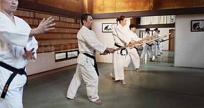 Aikido, group and fight class with sensei, weapon training and wooden sword for self defence exercise. Dojo, students and athlete in a gym or studio with workout, black belt practice and fitness