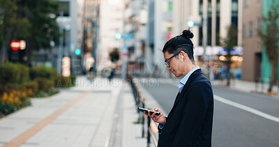 Buy stock photo Phone, networking and Japanese businessman in the city reading company email on technology. Career, travel and professional young male person scroll or browse on cellphone with earbuds in urban town.